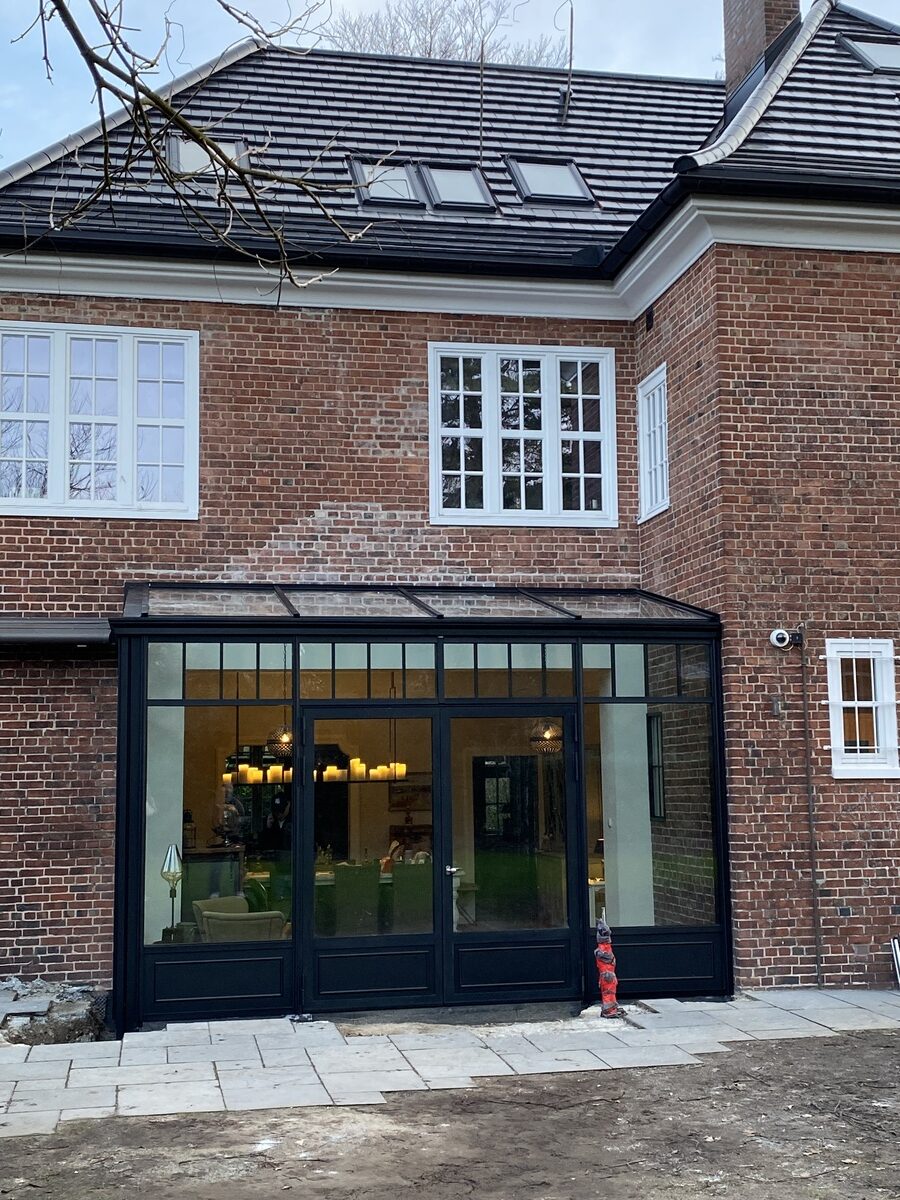 Backstein-Gebäude mit großen Glasfenstern, schwarzer Rahmen, moderne Lichtinstallationen im Inneren.