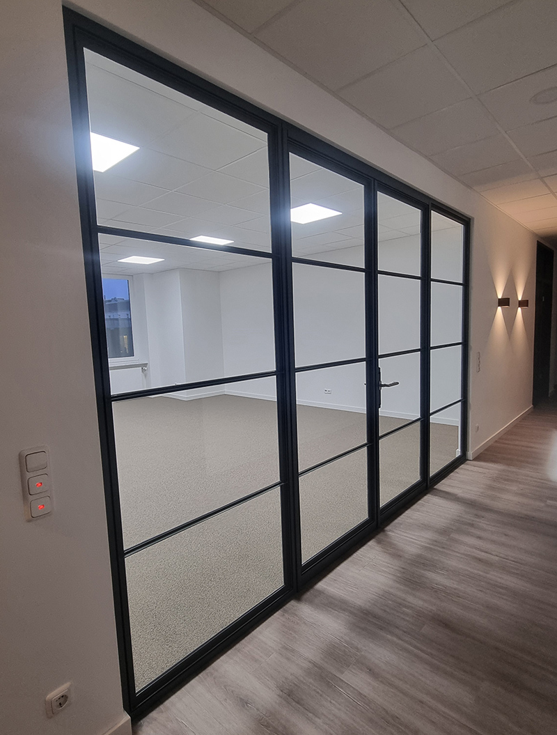 Eine moderne Glastür mit schwarzen Rahmen trennt zwei minimalistisch gestaltete Räume.