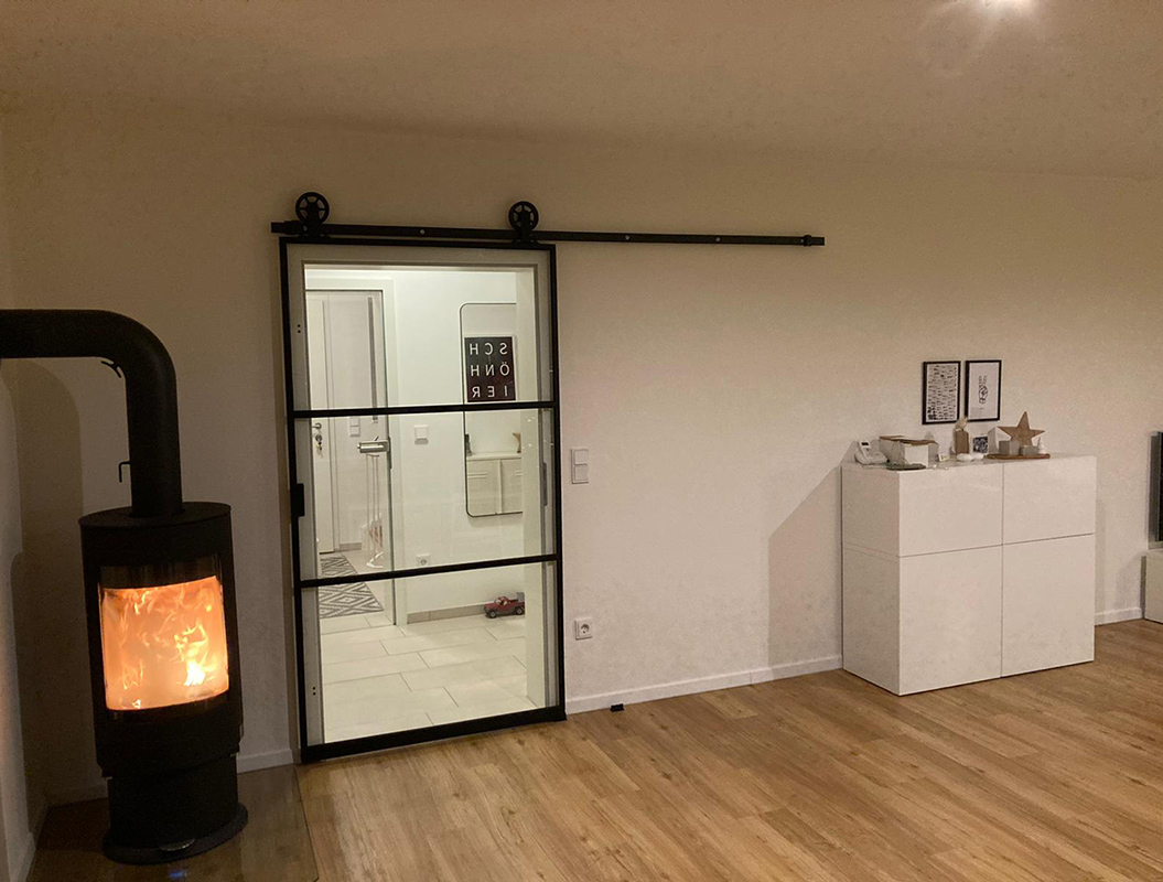Gemütlicher Raum mit Holzfußboden, Kaminofen, Glas-Schiebetür und weißem Schrank.