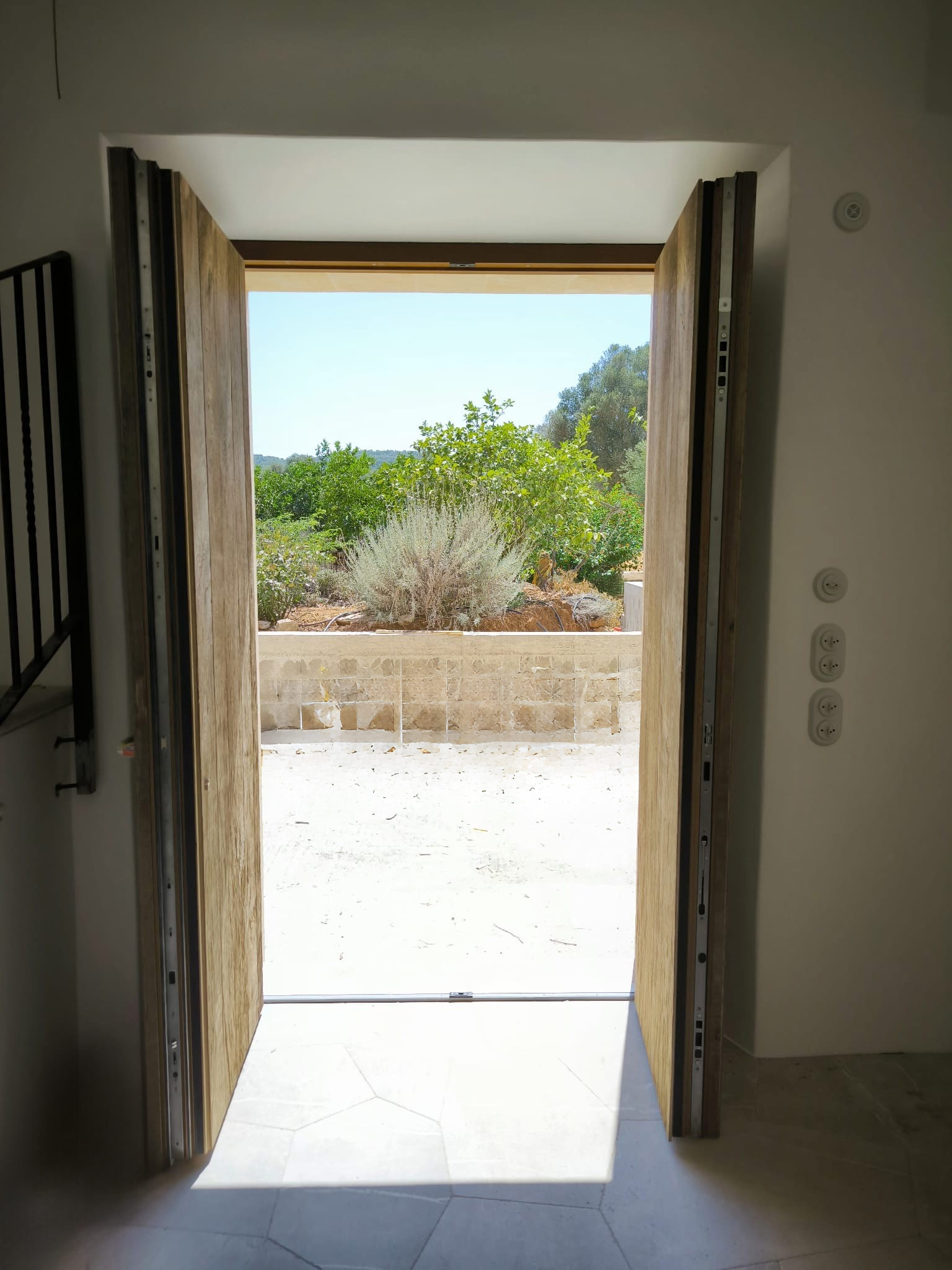 Offene Holztür mit Blick auf einen sonnigen Garten und grüne Pflanzen draußen