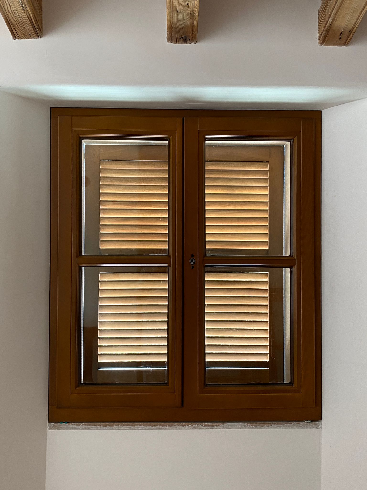 Ein geschlossenes Holzfenster, Licht dringt durch die Lamellen, helle Wände.