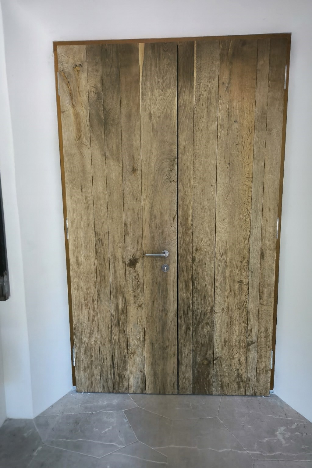 Holztür aus hellbraunen Brettern mit Metallgriff in schlichtem Rahmen
