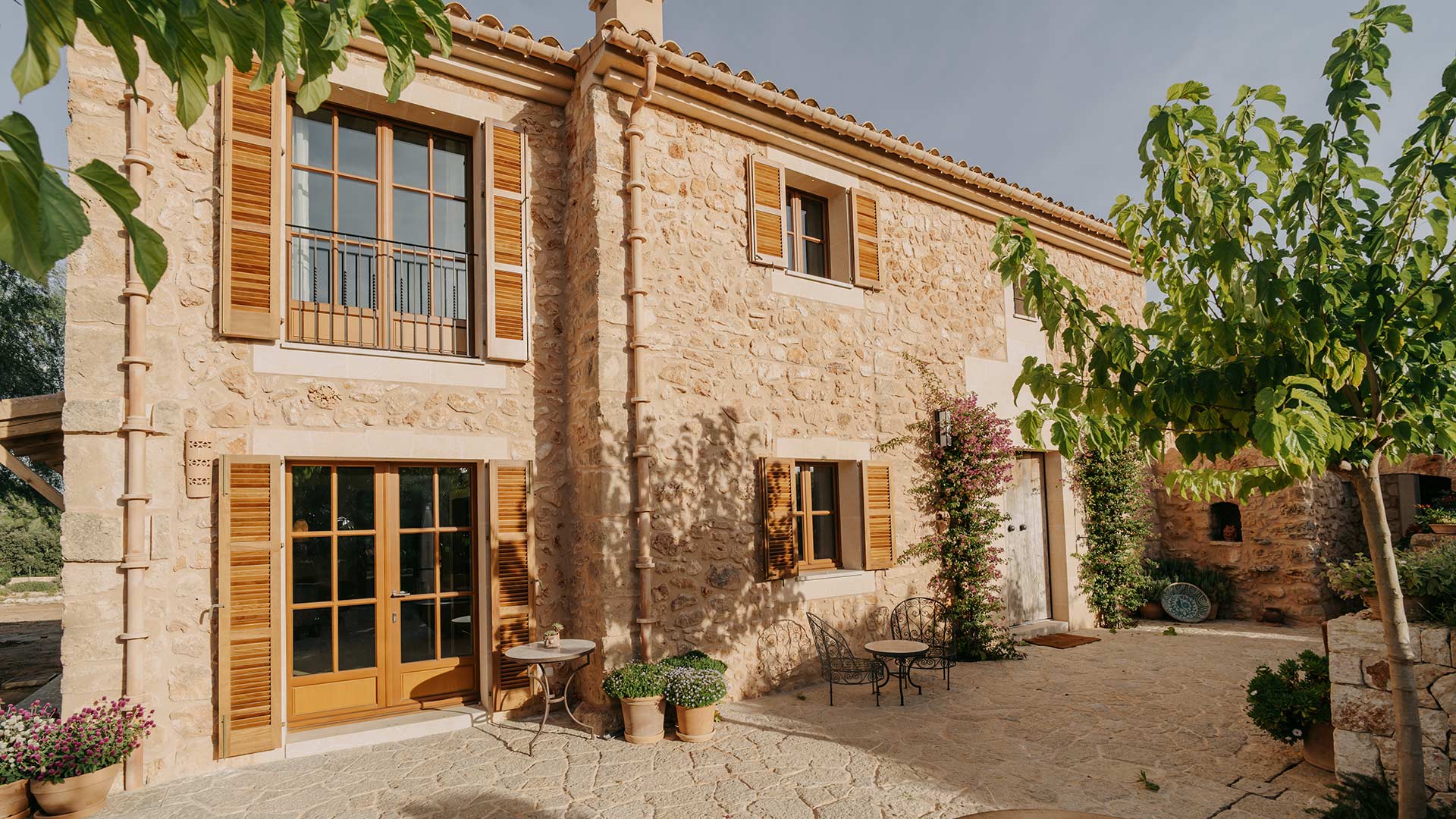 Steinernes Haus mit Holzfenstern, blühenden Pflanzen und sonnigem Innenhof