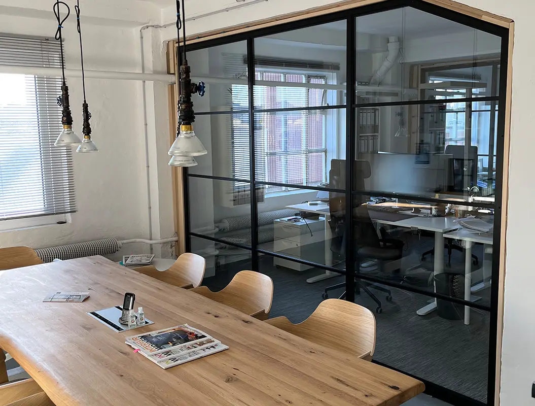 Helles Büro mit Holztisch und Glasraum, ruhig, schwarze Rahmen und Lampen