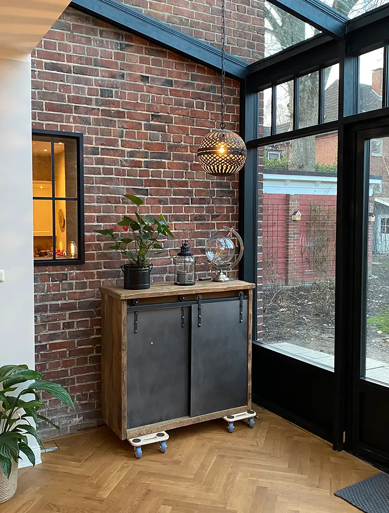 Pflanze auf Holzschrank, warme Lampe, rote Ziegelwand, Glasfenster rechts