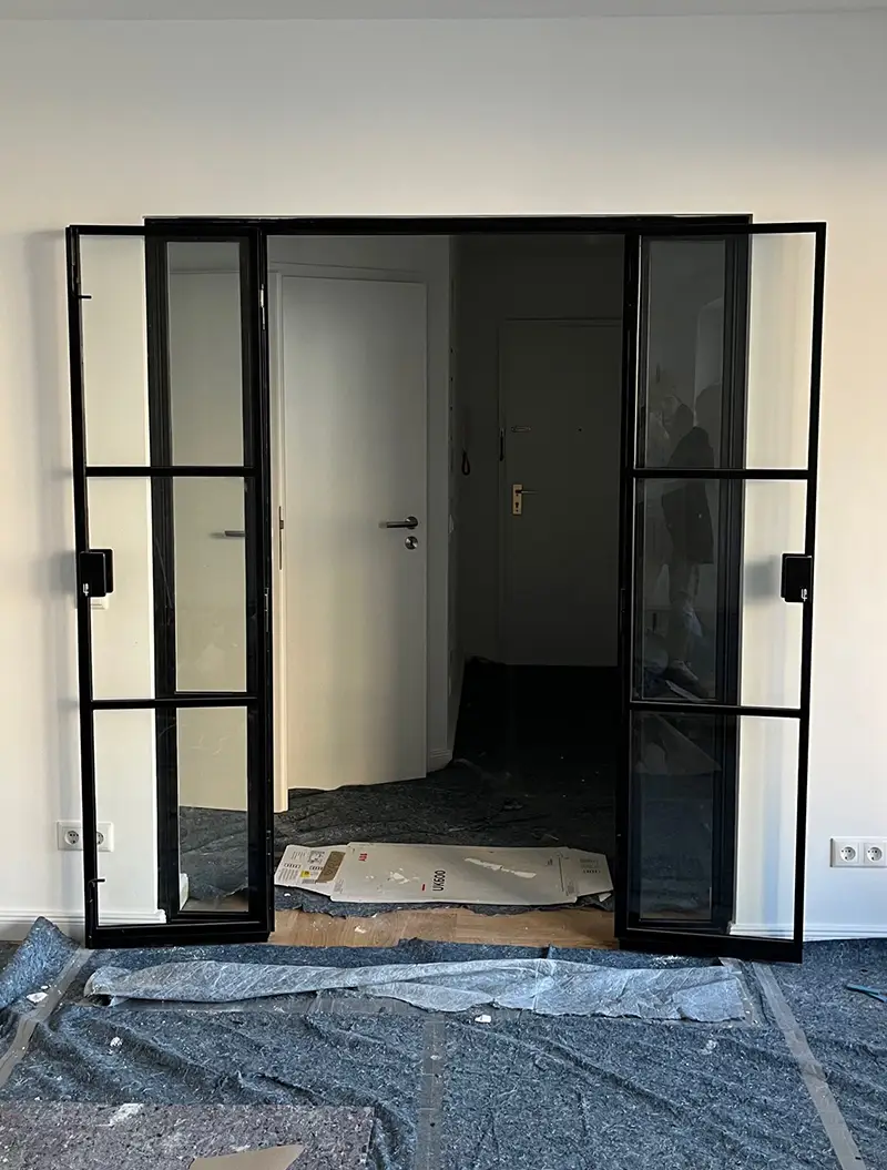 Schwarz gerahmte Glastuer im Raum, offen, Baustelle mit Folie am Boden